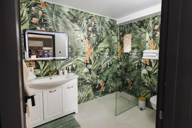 Baie modernă cu duș walk-in și tapet cu frunze tropicale
